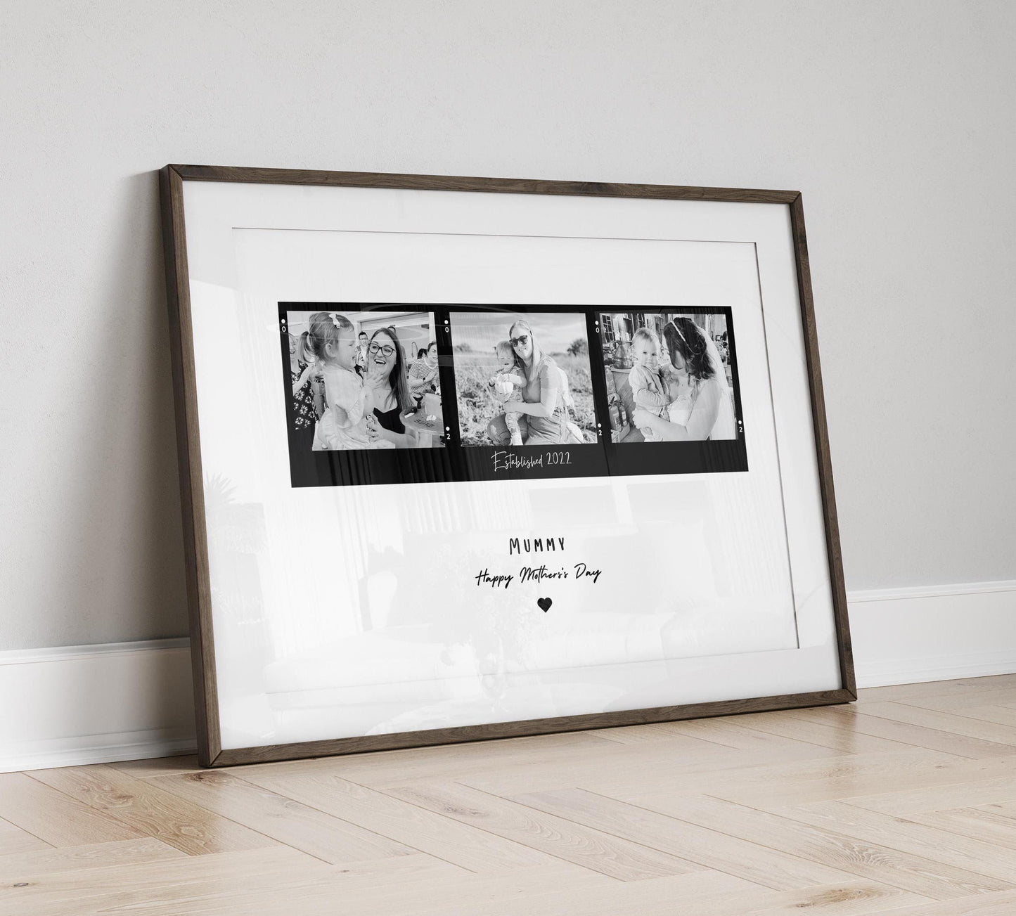 A framed black and white print featuring three candid mother-child photographs arranged in a film strip style. The center of the print includes the text "Established date." Below the images, Mum, Mummy, Mamma etc can be added. The frame can be black or white and the background is minimalistic.