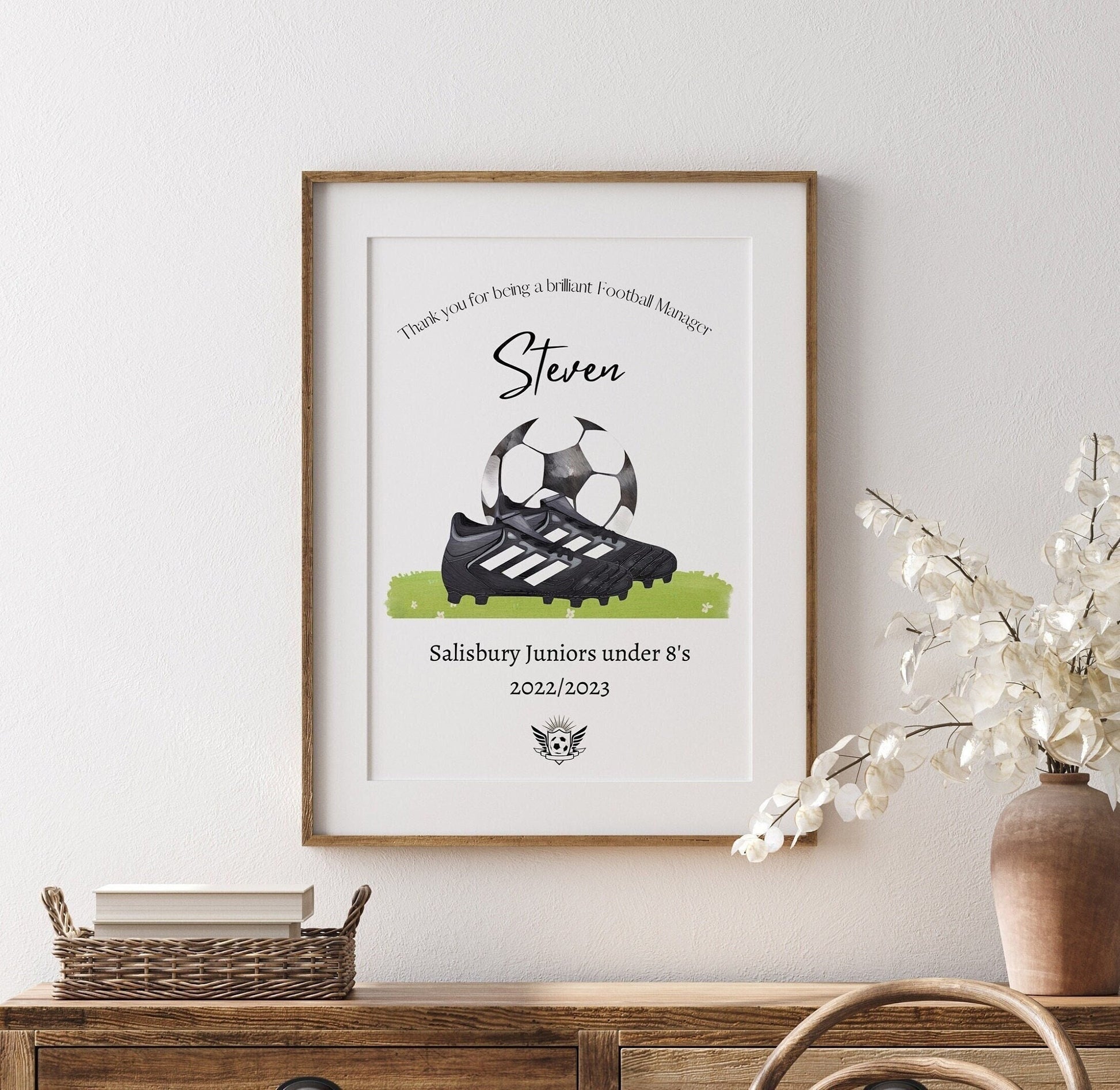 Personalised football print featuring the title ‘Coach’ or ‘Manager’ with the recipient’s name, team name, year, and team logo. The design includes a watercolour-style illustration of a football boot and ball, combining text and imagery in a sporty, artistic layout.